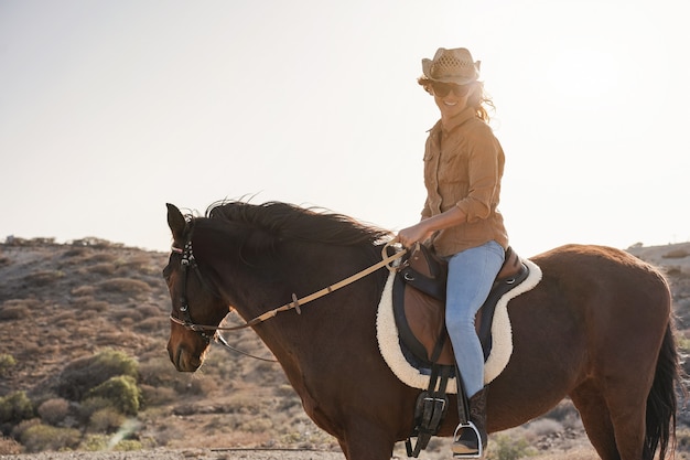 Jeune agricultrice montant son cheval dans une journée ensoleillée en plein air - Focus on face