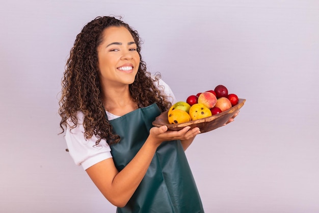 Jeune agricultrice tenant un bol avec des fruits. Mangue, pêche et pomme dans le panier dans la main de la fille