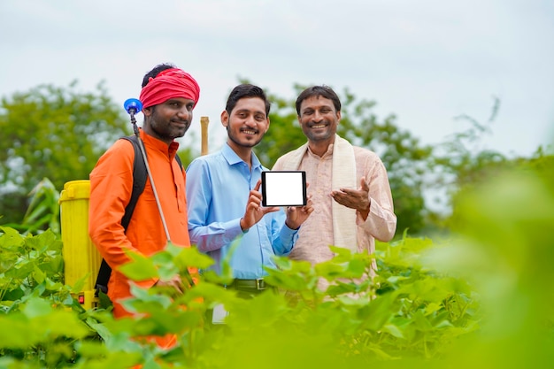 Jeune agronome ou banquier indien montrant un smartphone avec des agriculteurs dans un domaine agricole.