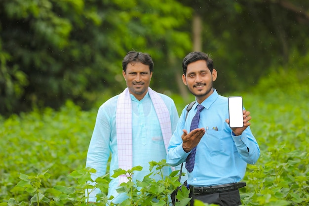 Jeune agronome ou banquier indien montrant un smartphone avec des agriculteurs dans un domaine agricole.