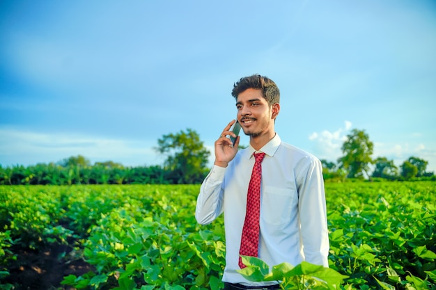 Jeune agronome beau indien parlant sur smartphone au champ