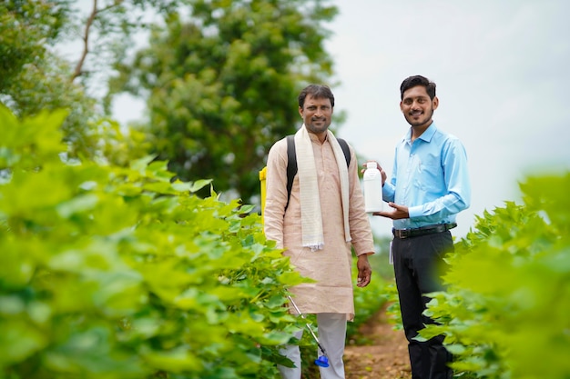 Jeune agronome indien donnant une bouteille d'engrais liquide à un agriculteur et disant des informations sur le produit sur le terrain de l'agriculture verte.