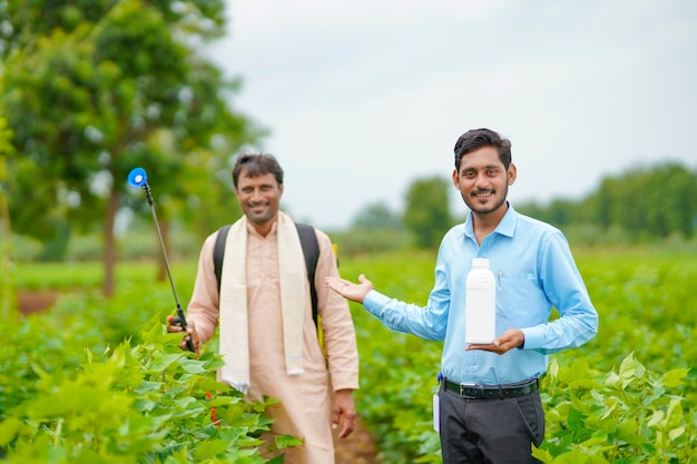 Jeune agronome indien donnant une bouteille d'engrais liquide à un agriculteur et disant des informations sur le produit sur le terrain de l'agriculture verte.