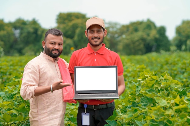 Jeune agronome indien montrant des informations à l'agriculteur dans un ordinateur portable dans un champ d'agriculture verte.