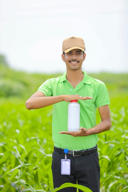 Jeune agronome indien tenant une bouteille d'engrais liquide dans un champ d'agriculture verte.