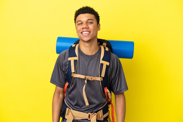 Jeune alpiniste afro-américain avec un gros sac à dos isolé sur fond jaune avec une expression faciale surprise