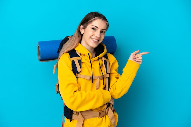 Jeune alpiniste femme avec un gros sac à dos isolé sur fond bleu doigt pointé sur le côté