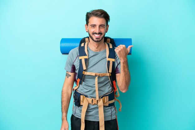 Jeune alpiniste avec un gros sac à dos isolé sur fond bleu pointant vers le côté pour présenter un produit