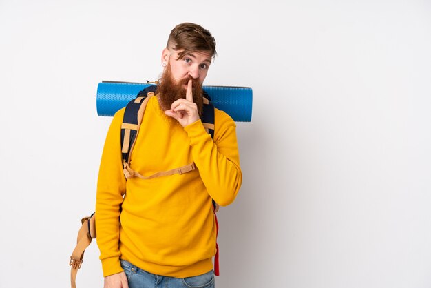 Jeune alpiniste avec un gros sac à dos sur un mur blanc faisant un geste de silence