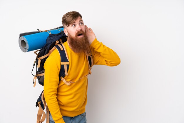 Jeune alpiniste avec un gros sac à dos sur un mur blanc isolé écouter quelque chose