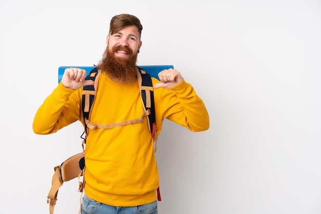 Jeune alpiniste avec un gros sac à dos sur un mur blanc isolé, fier et satisfait de lui-même