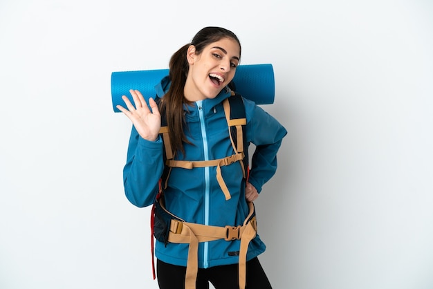 Jeune alpiniste avec un gros sac à dos sur un mur isolé saluant avec la main avec une expression heureuse