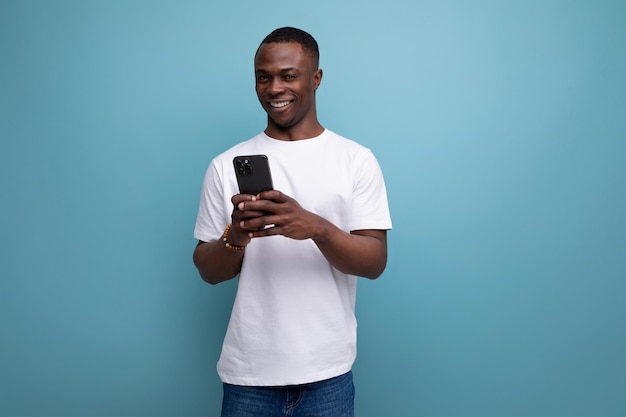 Un jeune Américain attrayant dans un T-shirt blanc avec un téléphone dans ses mains sur un fond de studio avec un espace de copie