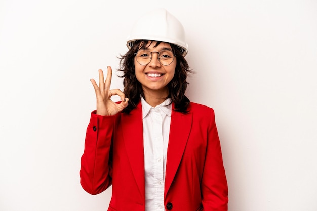 Jeune architecte femme hispanique avec casque isolé sur fond blanc gai et confiant montrant un geste ok