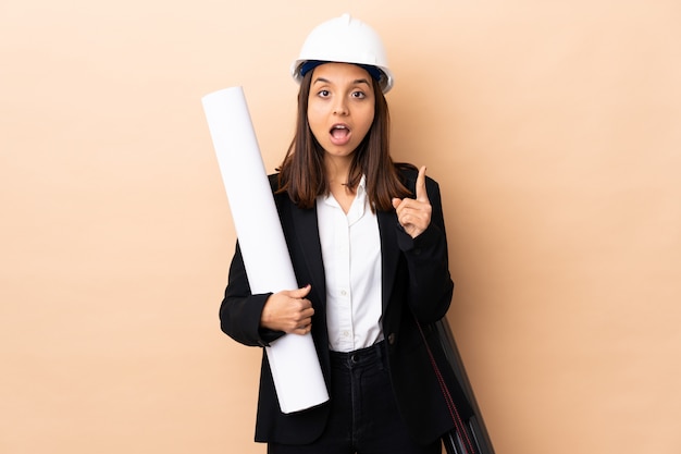 Jeune architecte femme tenant des plans sur fond isolé en pensant à une idée en pointant le doigt