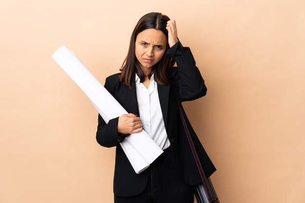 Jeune architecte femme tenant des plans sur le mur avec une expression de frustration et de ne pas comprendre