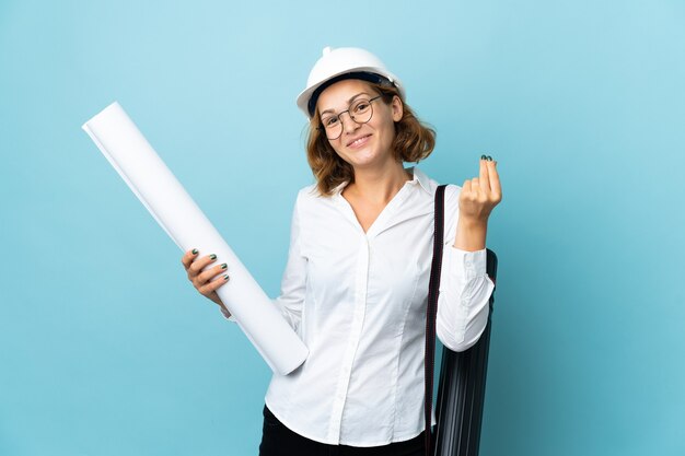 Jeune architecte géorgien femme avec casque et tenant des plans sur fond isolé faisant de l'argent geste