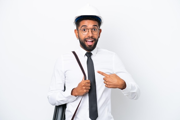 Jeune architecte homme brésilien avec casque et tenant des plans isolés sur fond blanc avec une expression faciale surprise