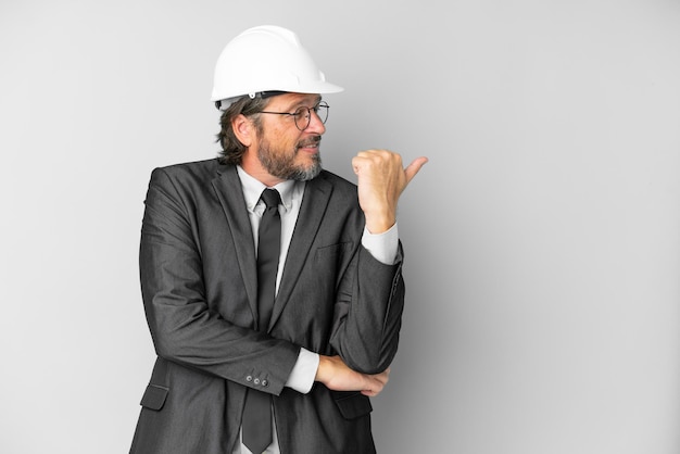 Jeune architecte homme avec casque sur fond isolé pointant vers le côté pour présenter un produit