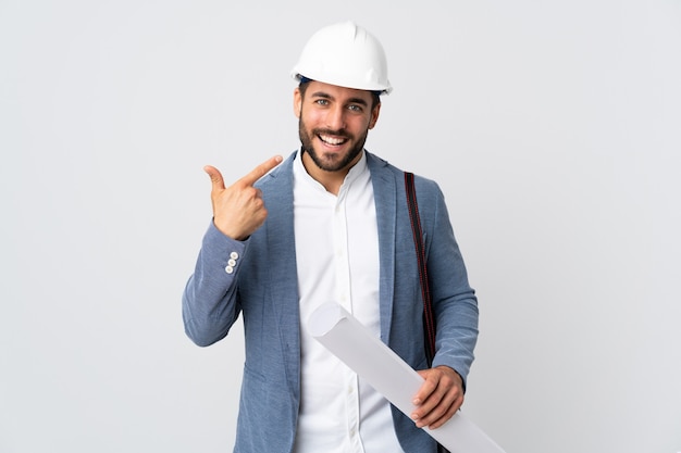 Jeune architecte homme avec casque et tenant des plans isolés sur mur blanc donnant un coup de pouce geste