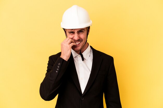 Jeune architecte homme caucasien isolé sur fond jaune se rongeant les ongles, nerveux et très anxieux.