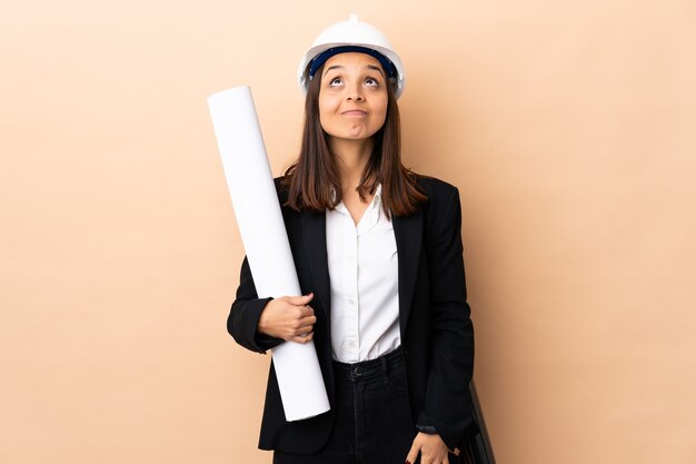 Jeune architecte woman holding blueprints sur mur isolé et levant