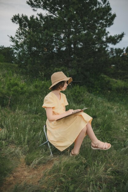 jeune artiste de 1013 ans vêtue d'une robe jaune et d'un chapeau de paille dans la nature peignant un tableau