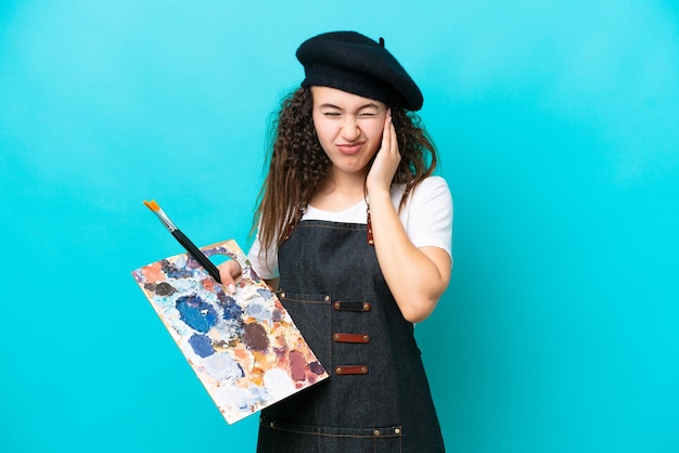 Jeune artiste arabe femme tenant une palette isolée sur fond bleu frustré et couvrant les oreilles