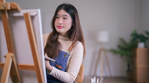 Une jeune artiste asiatique utilisant un pinceau avec une palette de couleurs pour créer des œuvres d'art sur toile