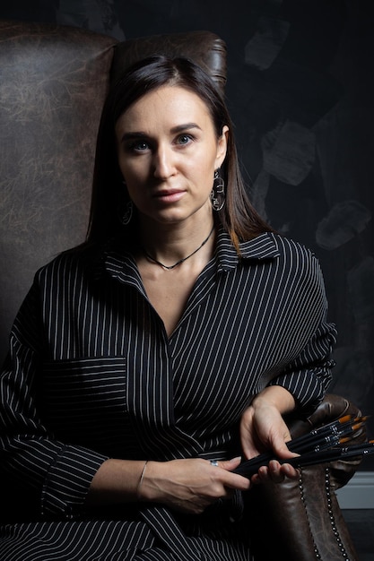 une jeune artiste brune se tient derrière une séance photo de chevalet sur un fond noir dans le studio