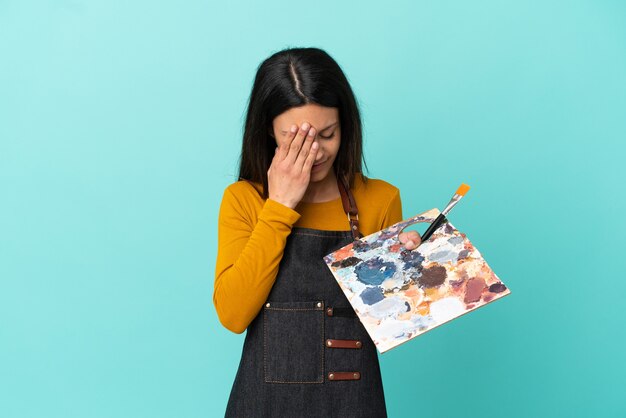 Jeune artiste femme caucasienne tenant une palette isolée sur fond bleu avec une expression fatiguée et malade