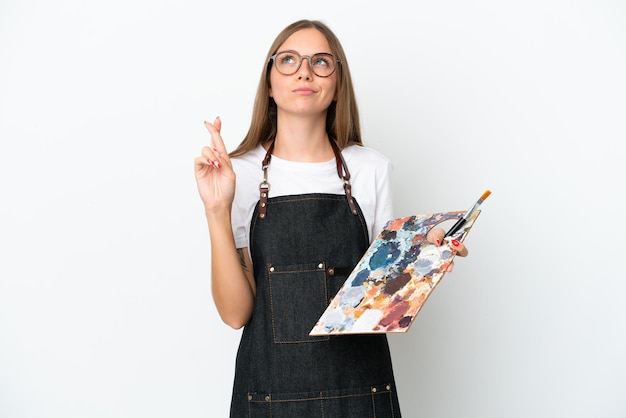 Jeune artiste femme lituanienne tenant une palette isolée sur fond blanc avec les doigts croisés et souhaitant le meilleur