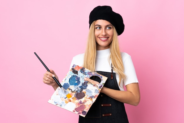 Jeune artiste femme tenant une palette sur un espace rose isolé