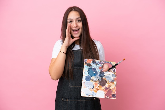 Jeune artiste femme ukrainienne tenant une palette isolée sur fond noir avec une expression faciale surprise et choquée