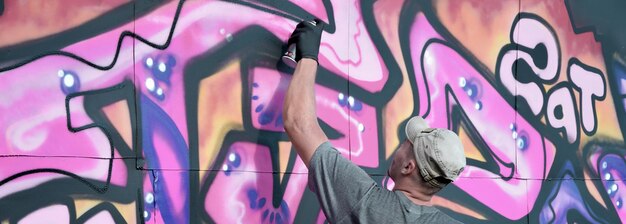 Jeune artiste de graffiti masculin caucasien dessinant une grande peinture d'art de rue dans des tons bleus et roses