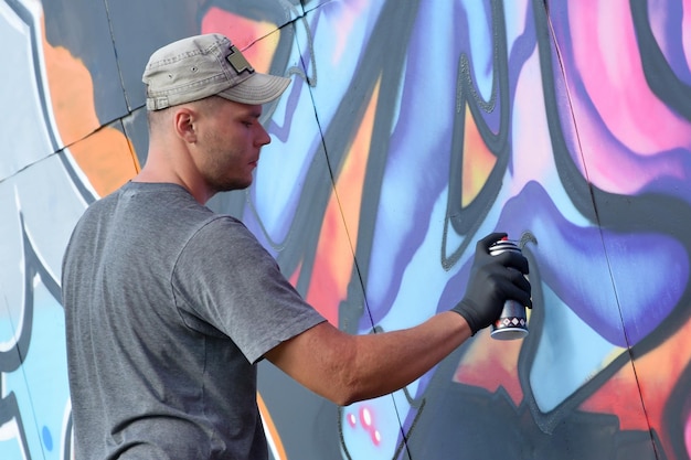 Jeune artiste de graffiti masculin caucasien dessinant une grande peinture d'art de rue dans des tons bleus et roses