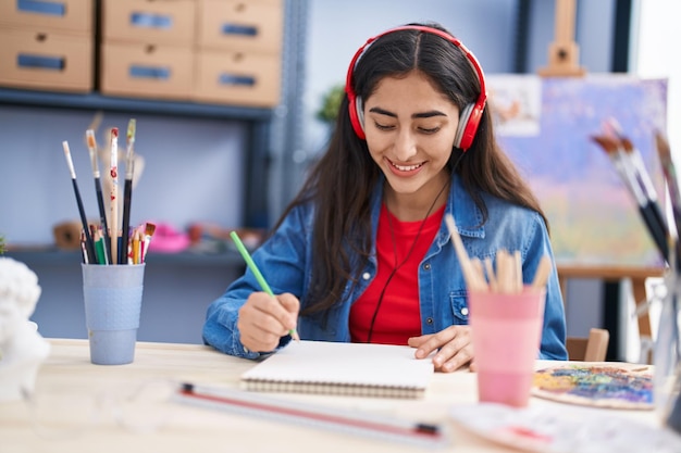 Jeune artiste hispanique écoutant de la musique dessinant sur un ordinateur portable au studio d'art