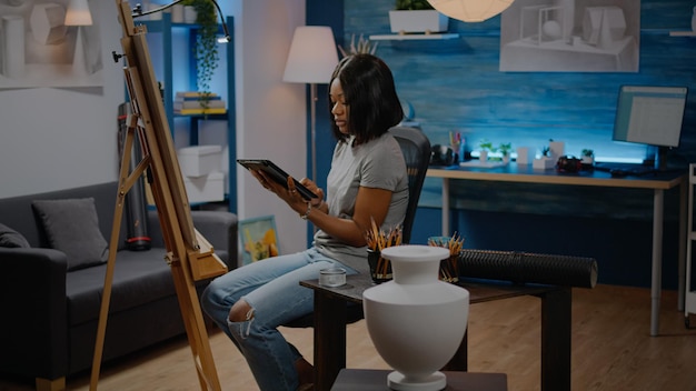 Jeune artiste noir tenant une tablette numérique pour un dessin de vase dans un studio d'art. Femme afro-américaine utilisant la technologie moderne à la recherche d'inspiration pour le prochain projet de chef-d'œuvre sur toile