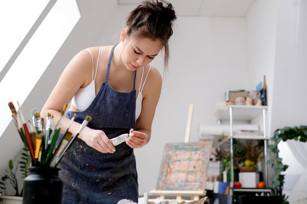 Une jeune artiste peint un tableau à l'huile sur toile dans un studio d'art
