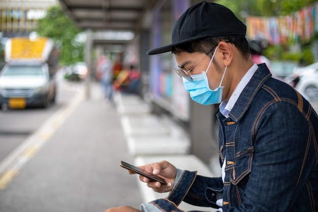 Jeune asiatique à l'aide d'un téléphone intelligent dans la ville et portant un masque facial pour la protection