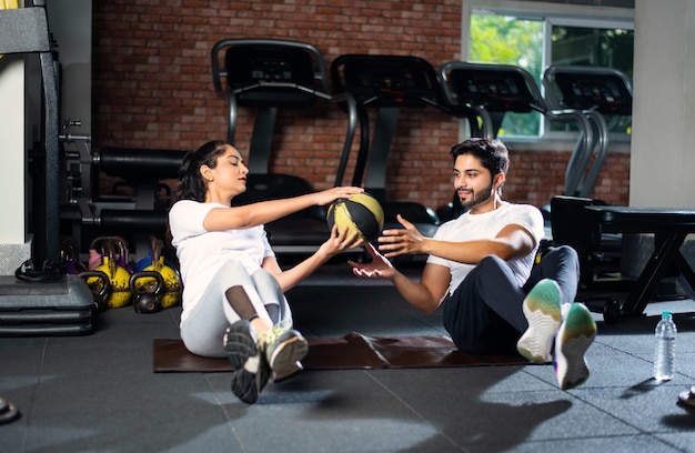 Jeune asiatique indien Fit couple faisant des exercices en se passant le ballon sur un tapis de yoga au sol.