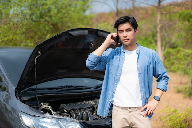 Jeune asiatique malheureux homme parlant sur un téléphone portable devant le capot ouvert en panne de voiture sur la route de campagne téléphoner pour obtenir de l'aide.