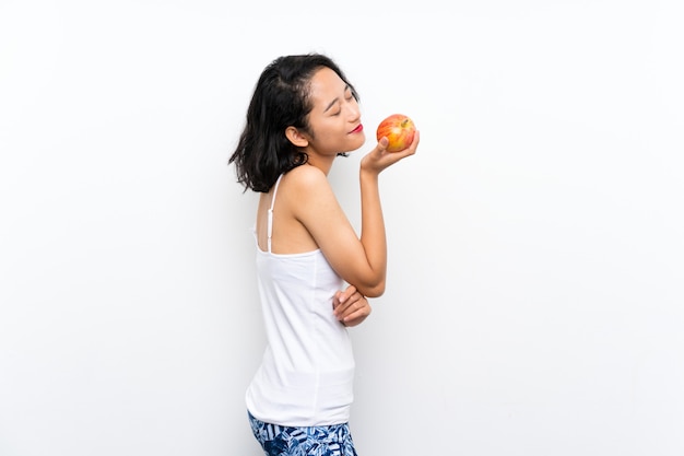 Jeune asiatique avec une pomme sur un mur blanc isolé