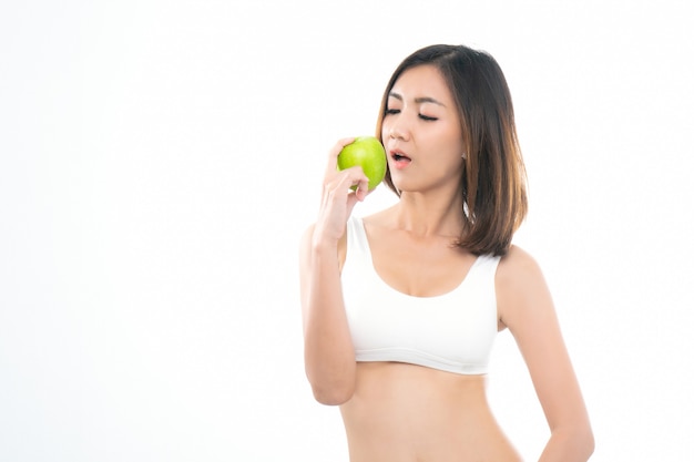 Jeune asiatique en soutien-gorge de sport blanc mange une pomme verte.