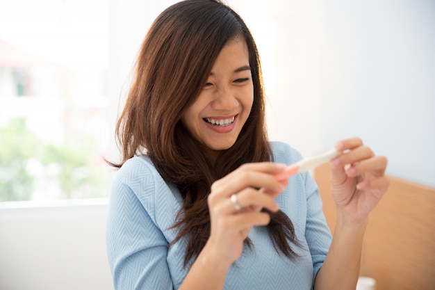 Jeune asiatique avec un testpack à la main, souriant joyeusement