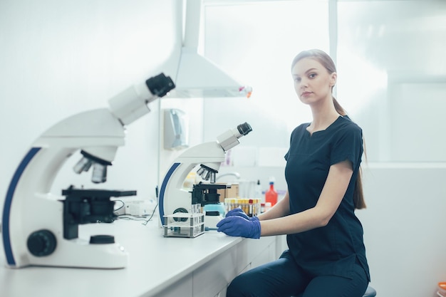 Jeune assistant de laboratoire assis dans le laboratoire moderne et travaillant avec des échantillons