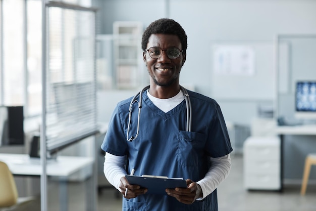Un jeune assistant souriant en tenue médicale bleue tenant un document
