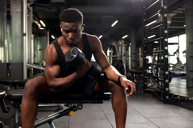 Un jeune athlète afro-américain s'entraîne dans un gymnase sombre. Un athlète soulève des haltères lourds.