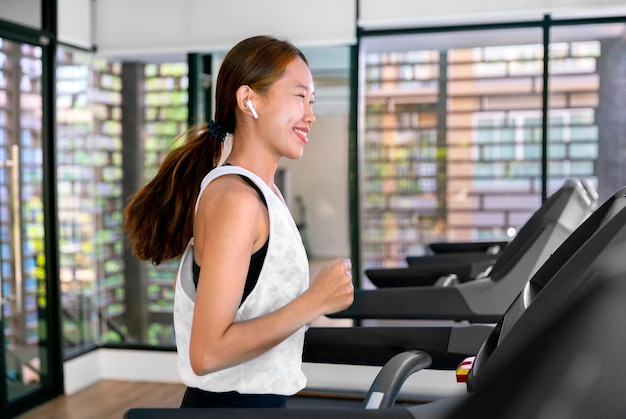 Jeune athlète asiatique heureuse courir sur un tapis roulant en cours d'exécution dans une salle de sport intérieure fitness pour la santé