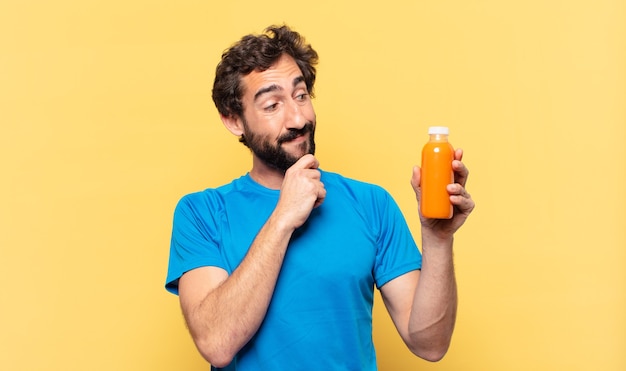 Jeune athlète barbu fou pensant l'expression et tenant un smoothy